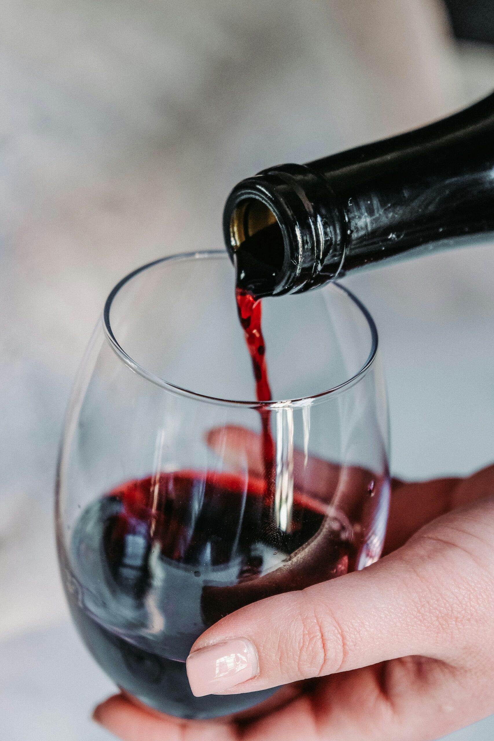 Czerwone wino bezalkoholowe nalewane z butelki do dużego szklanego kieliszka trzymanego przez kobiecą dłoń.