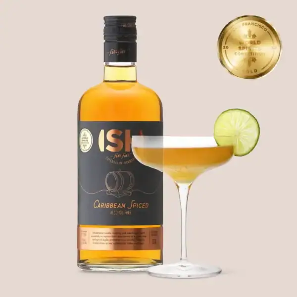 Butelka bezalkoholowego alternatywnego rumu ISH Caribbean Spiced Spirit obok eleganckiego kieliszka z koktajlem ozdobionym plasterkiem limonki.