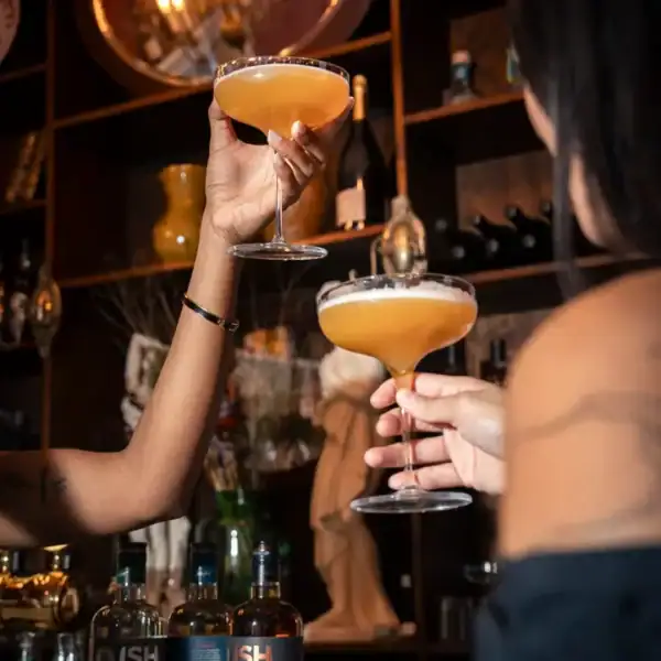 Dwie osoby wznoszą toast eleganckimi kieliszkami z drinkami przygotowanymi na bazie bezalkoholowego rumu ISH Caribbean Spiced Spirit.
