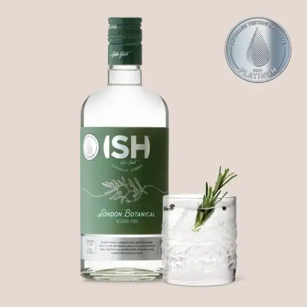 Butelka bezalkoholowego ginu ISH London Botanical obok szklanki z gotowym drinkiem z lodem i rozmarynem na beżowym tle.