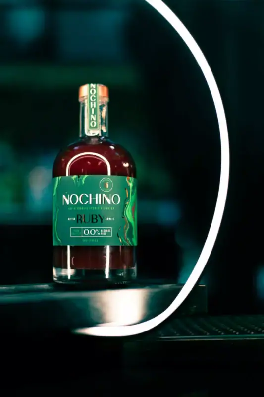 Butelka bezalkoholowego aperitifu Nochino Ruby wyeksponowana na nowoczesnym, ciemnym tle z jasnym, neonowym podświetleniem