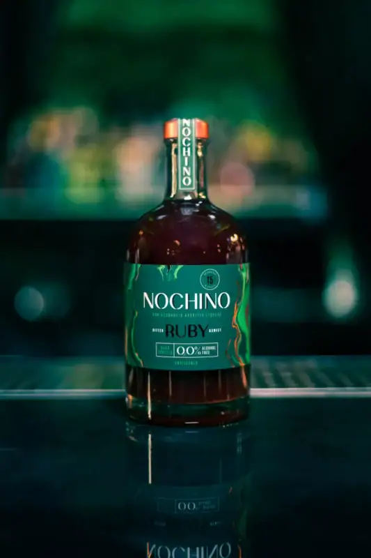 Bezalkoholowy aperitif Nochino Ruby w eleganckiej szklanej butelce zaprezentowany na ciemnym, nastrojowym tle.